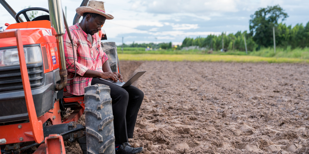 farmer sitting on tractor in farmfield using laptop computer 