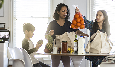Woman and two children unpacking grocery bags in kitchen