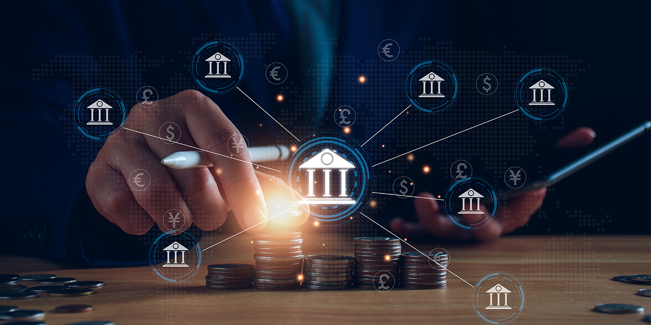 Icons of financial institutions and various currencies connected by lines overlayed on a desk with stacked coins and a person's hand picking up a coin